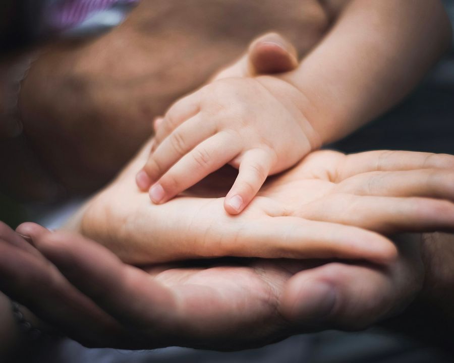 Mãos de pais segurando a mão de um bebê simbolizando proteção familiar